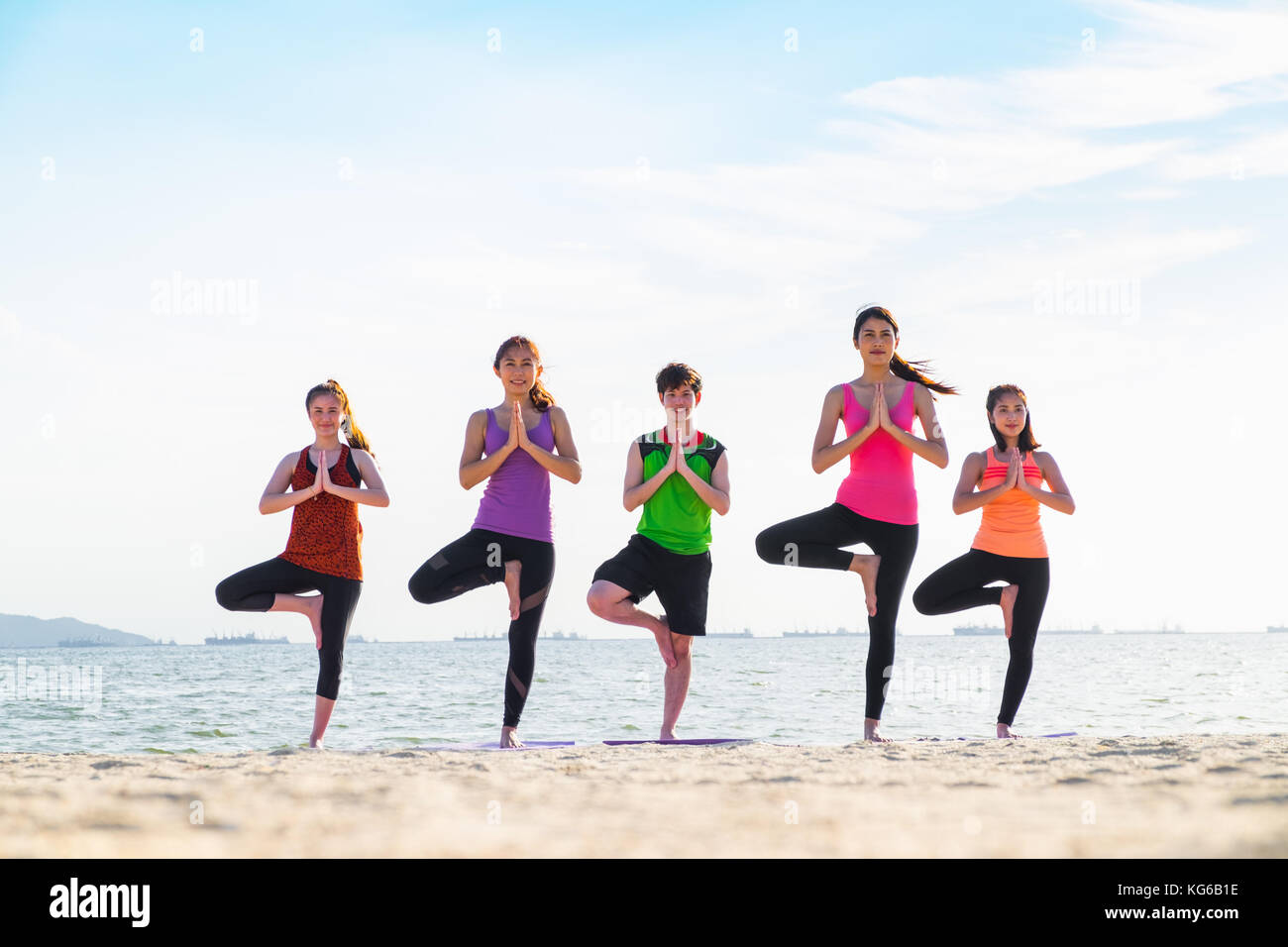 Yoga di gruppo di persone facendo la posizione dell'albero e namaste con calma relax emozione a beach,meditazione pongono,benessere e uno stile di vita sano Foto Stock