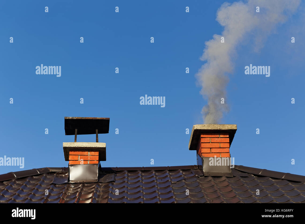 Fumo dalla ciminiera in mattoni sul tetto contro il cielo blu Foto Stock