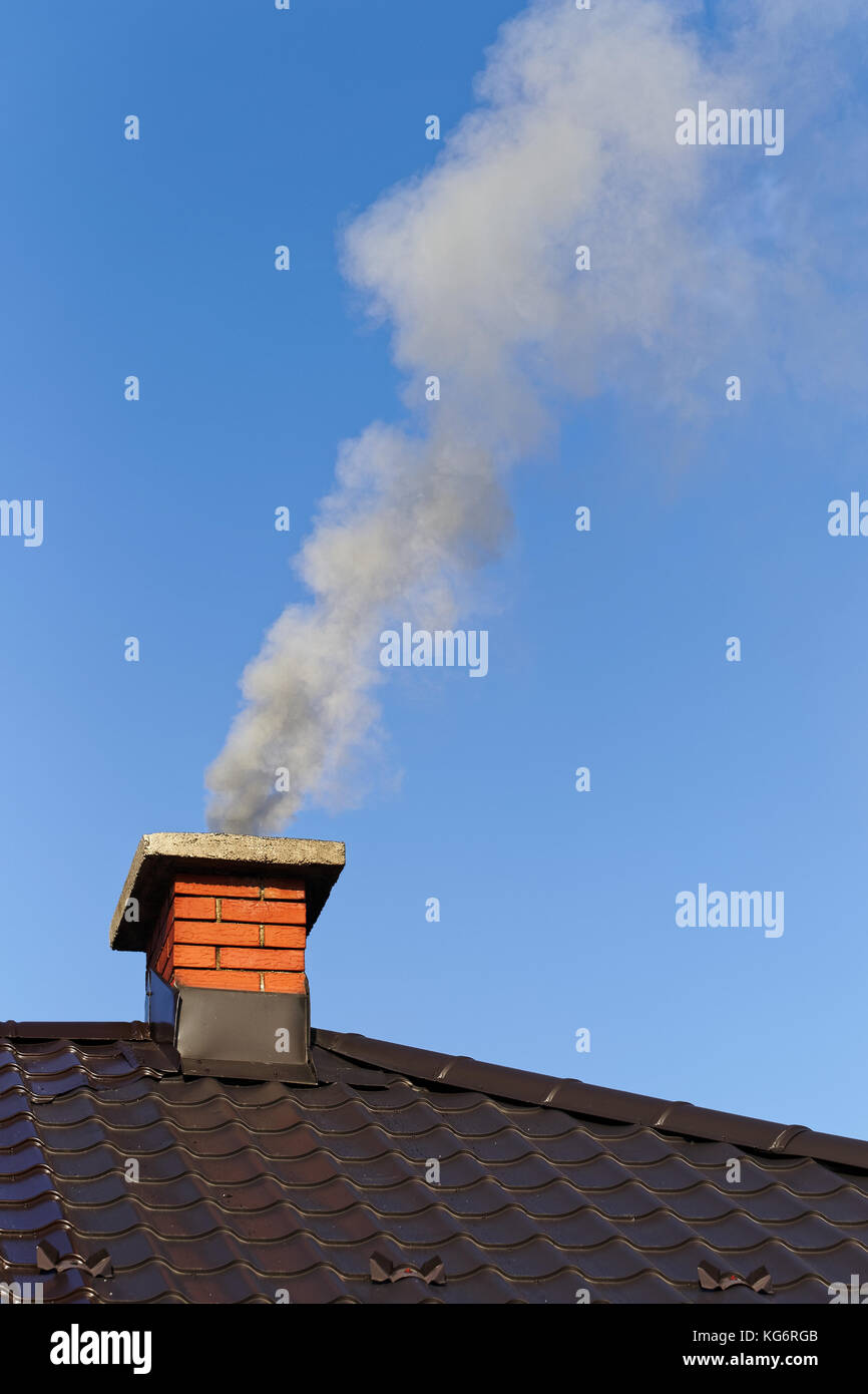 Fumo dalla ciminiera in mattoni sul tetto contro il cielo blu Foto Stock