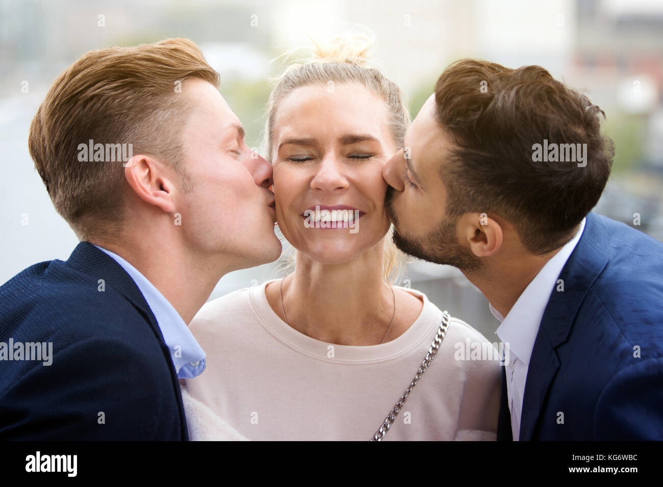 Ritratto di due giovani uomini baciare donna bionda sulle sue guance Foto Stock