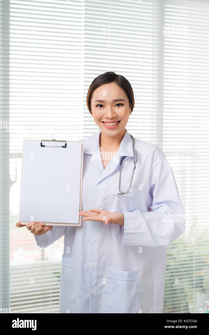 Giovani asiatici medico donna sconvolto il punto a vuoto appunti mentre si sta in piedi in ospedale Foto Stock