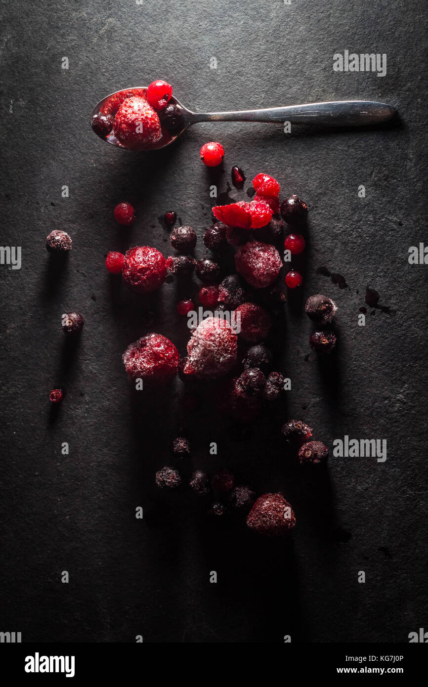 Misto di frutti di bosco selvatici sat su un livello di grigio ardesia piatto di portata spolverati di zucchero con un cucchiaio di lucido Foto Stock