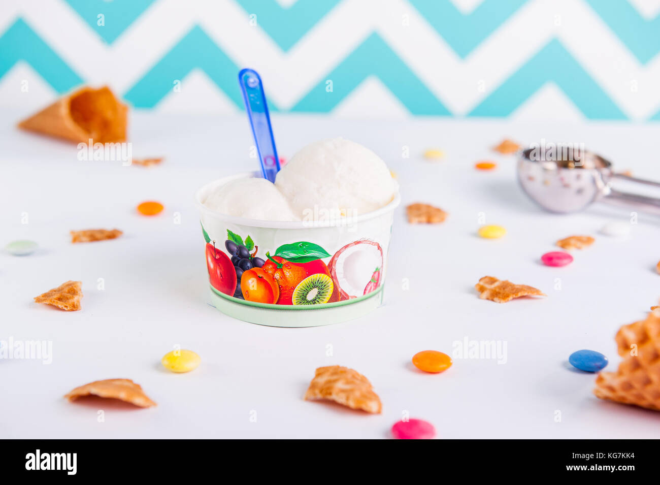 Close up con gelato alla vaniglia in un bicchiere di carta su sfondo bianco con caramelle colorate, pezzi di cialde, gelato cucchiaio e vuoto cono gelato. Foto Stock