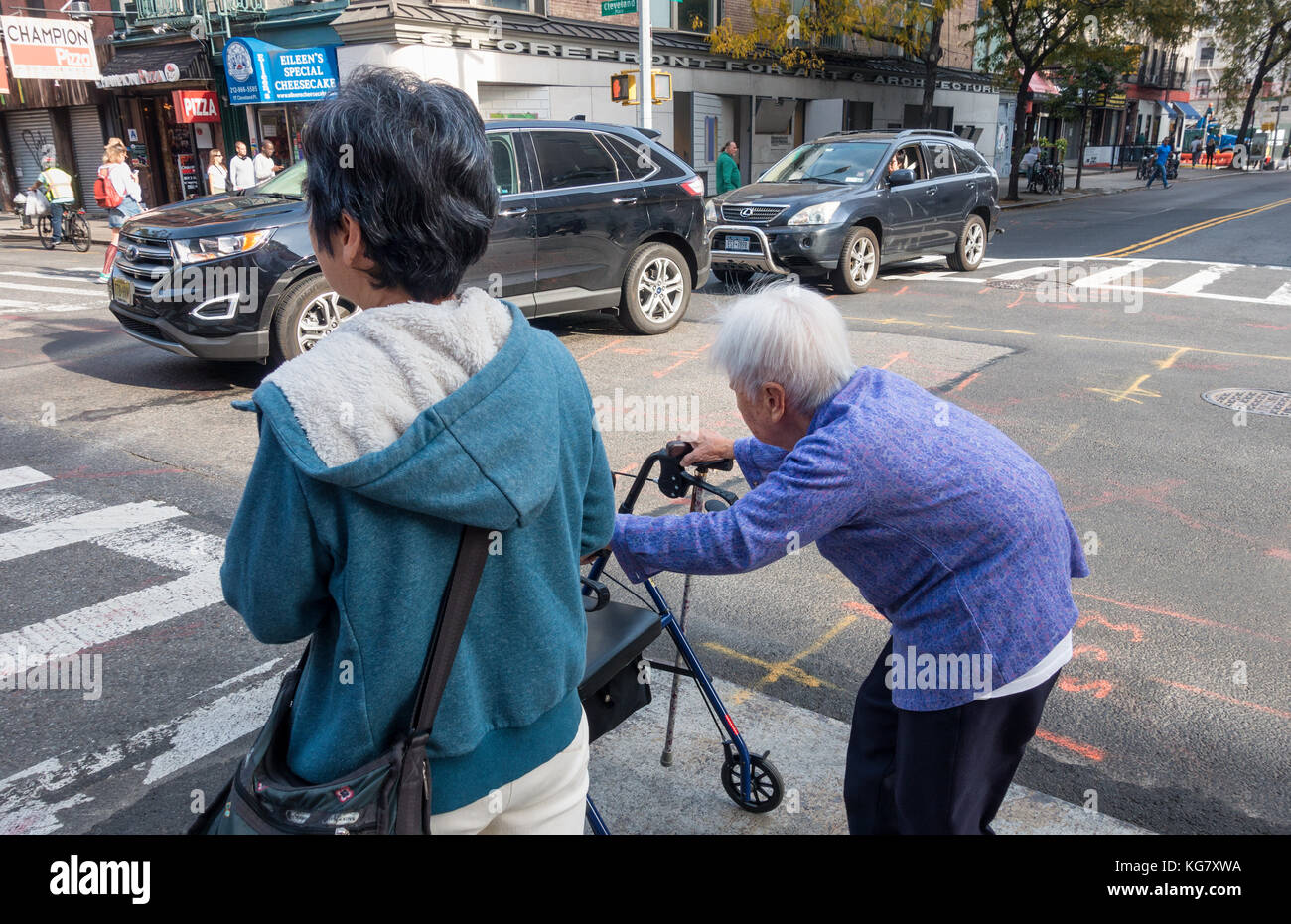 Donna anziana su un camminatore accompagnato dal suo custode a New York City Foto Stock