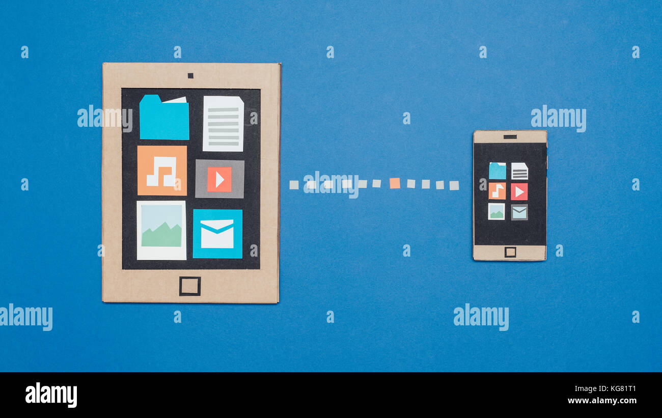 I dispositivi portatili che si connettono: la sincronizzazione dei dati e il trasferimento di file, creative smartphone e tablet realizzata in cartone riciclato Foto Stock