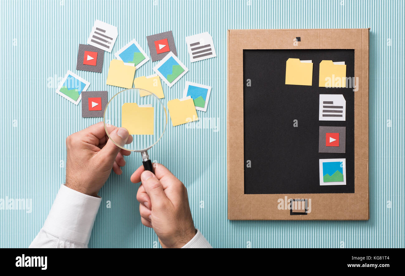 Per la selezione dei file, la gestione e l'organizzazione: utente analisi di carta tagliato le cartelle con una lente di ingrandimento e aggiungendo al suo cartone schermo tablet Foto Stock
