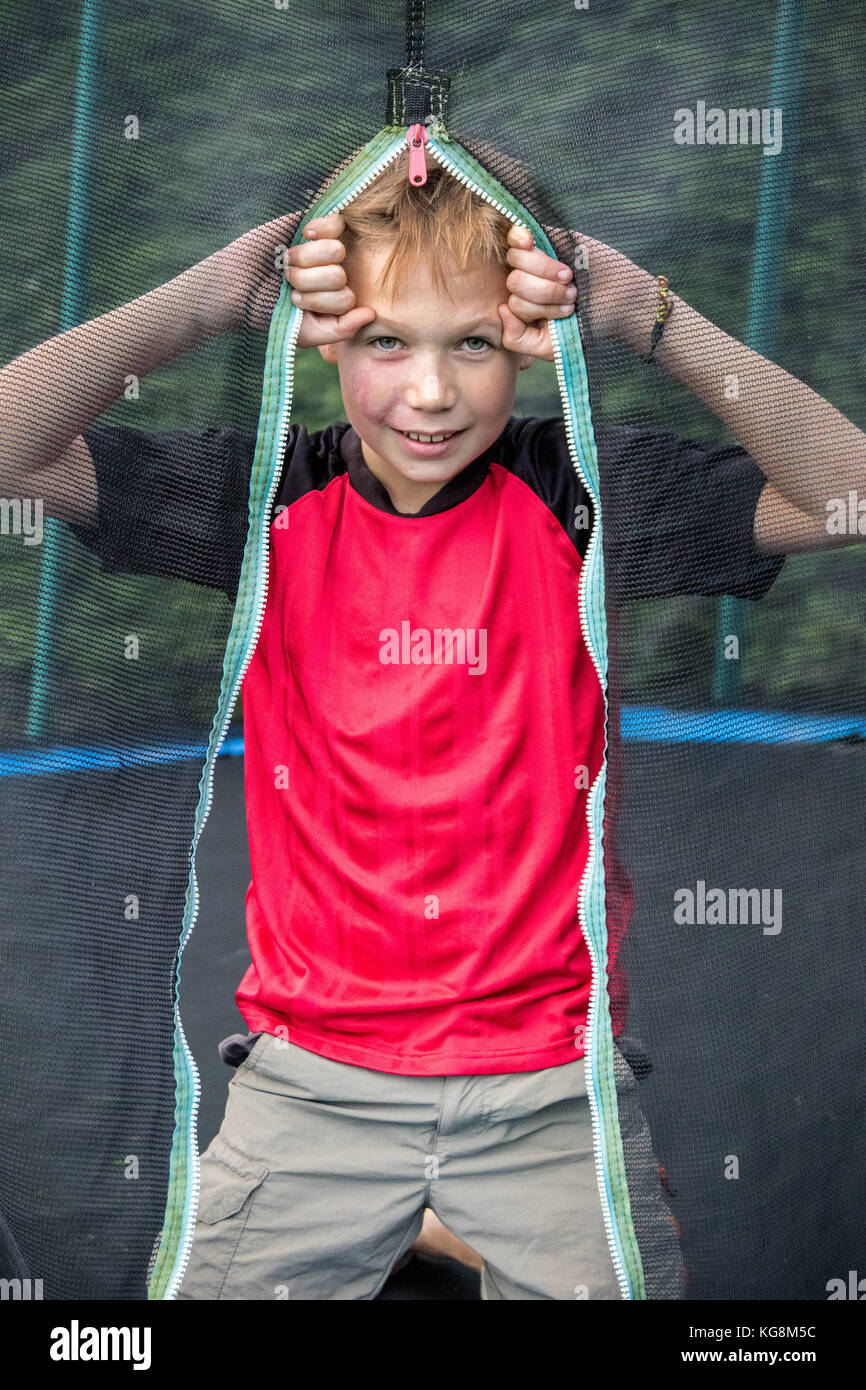 Cheeky pre-teen boy guardando attraverso il trampolino net al di fuori Foto Stock