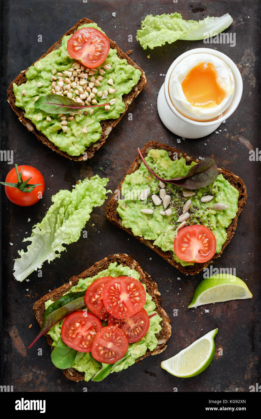 Verde sano veggie toast con avocado, pomodoro, i germogli e i semi e uova sode su sfondo arrugginito. Tabella vista dall'alto. Cibo sano, dieta vegana concep Foto Stock