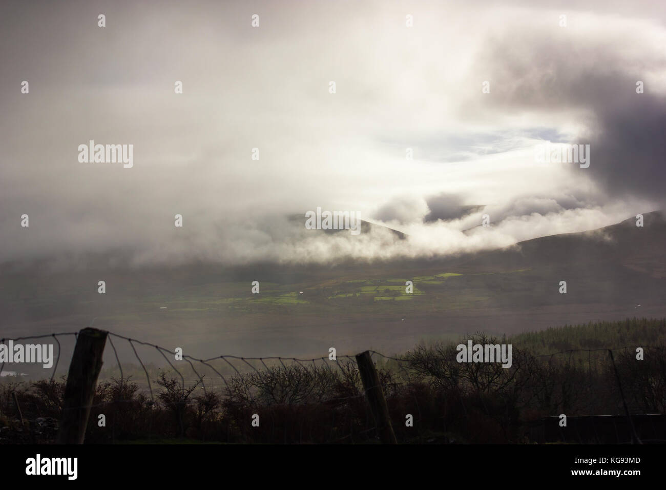 Vista la riva del mare in Irlanda pioggia nuvole appesa sopra le montagne e il cielo blu, Sun mostra dal cloud campi verde fiume Foto Stock