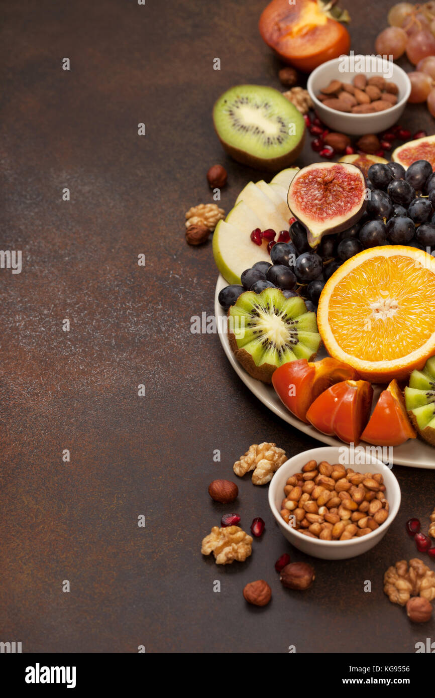 Piatto con frutta fresca e i dadi: arancione, uva da tavola, kiwi, kaki, fichi, mandorle, noci, pinoli su sfondo scuro Foto Stock