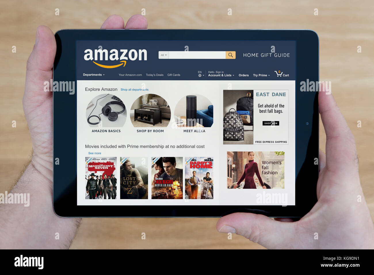 Un uomo guarda al sito web di Amazon sul suo iPad dispositivo tablet, sparato contro un tavolo di legno top sfondo (solo uso editoriale) Foto Stock