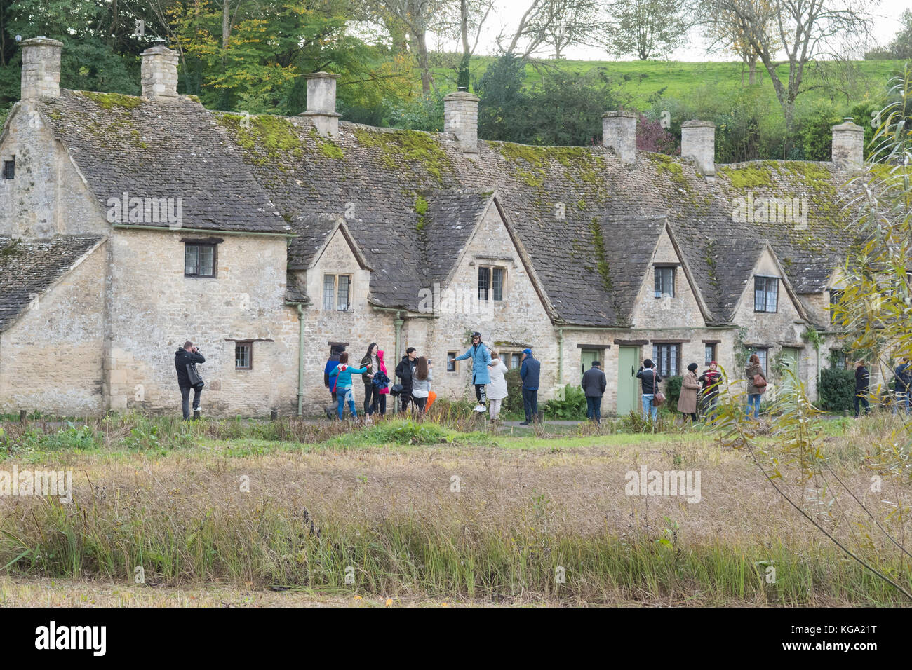 I turisti che scattano fotografie fuori Arlington Row - una fila popolare di cottage di Cotswold nel villaggio grazioso di Cottswold di Bibury, Inghilterra, Regno Unito Foto Stock