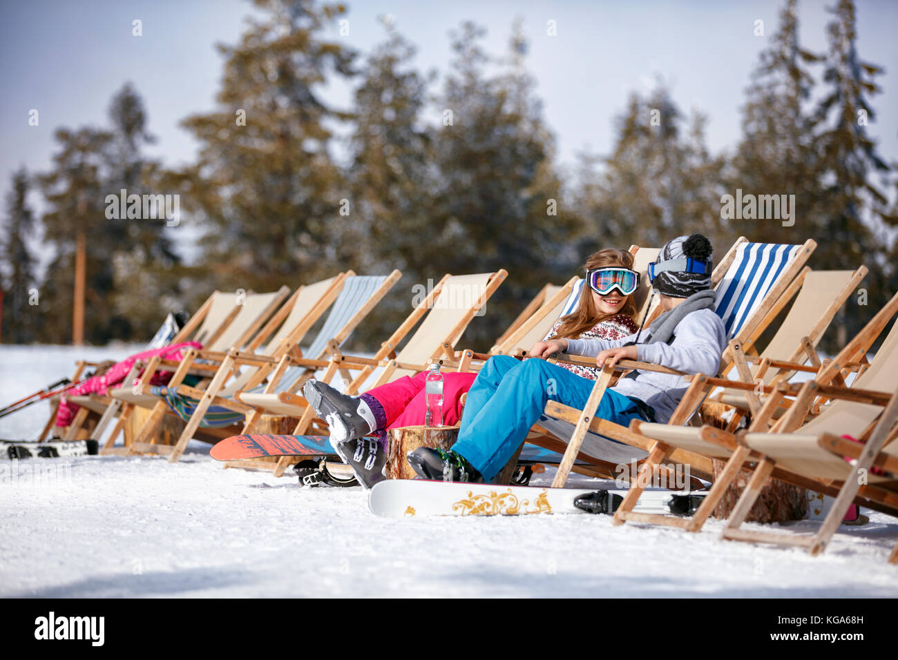 Dei bambini felici in montagne in inverno a ridere e rilassarsi in prendisole sedie Foto Stock