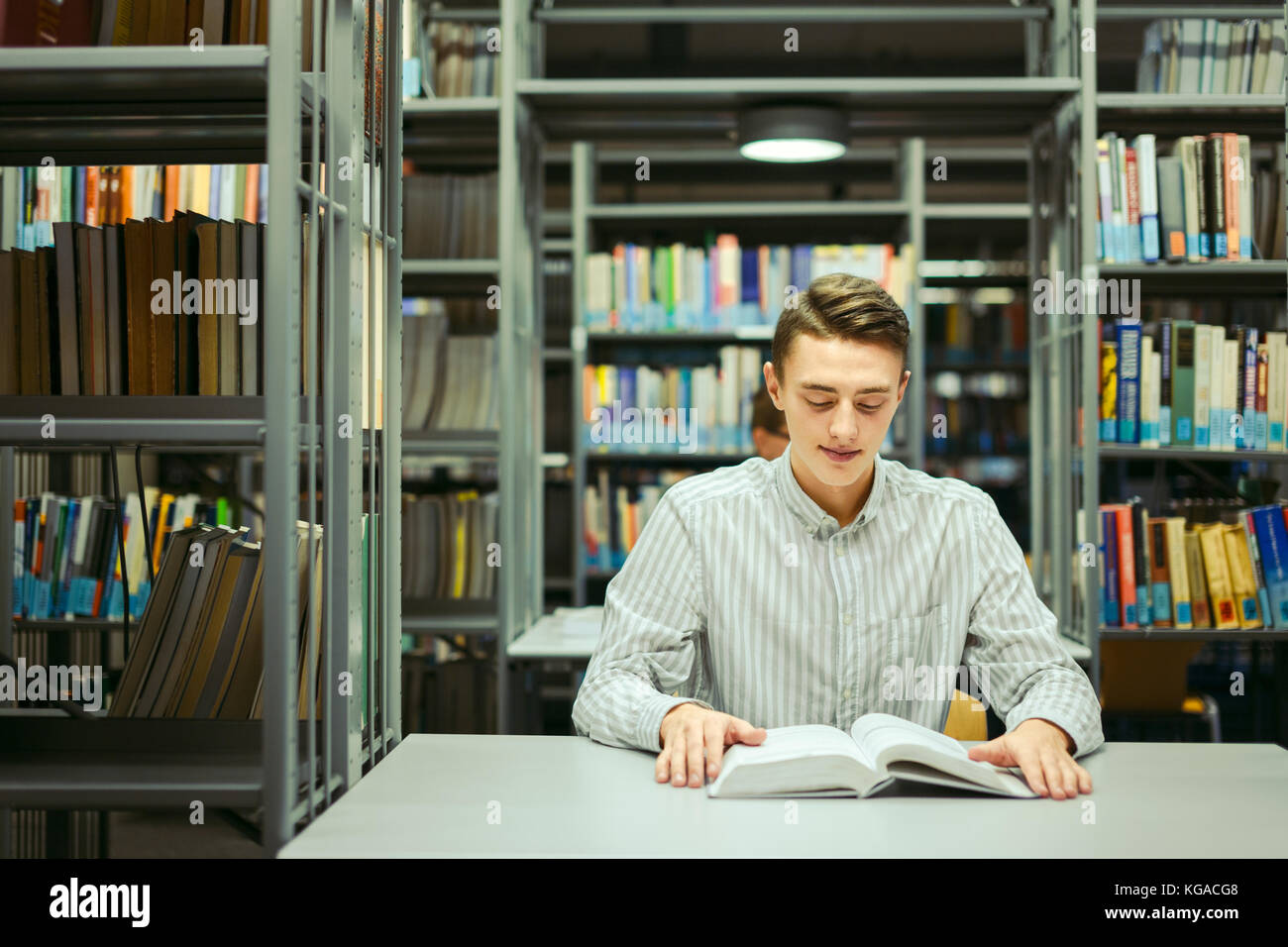 Uomo seduto sulla biblioteca e leggere il libro con la sfocatura sullo sfondo Foto Stock