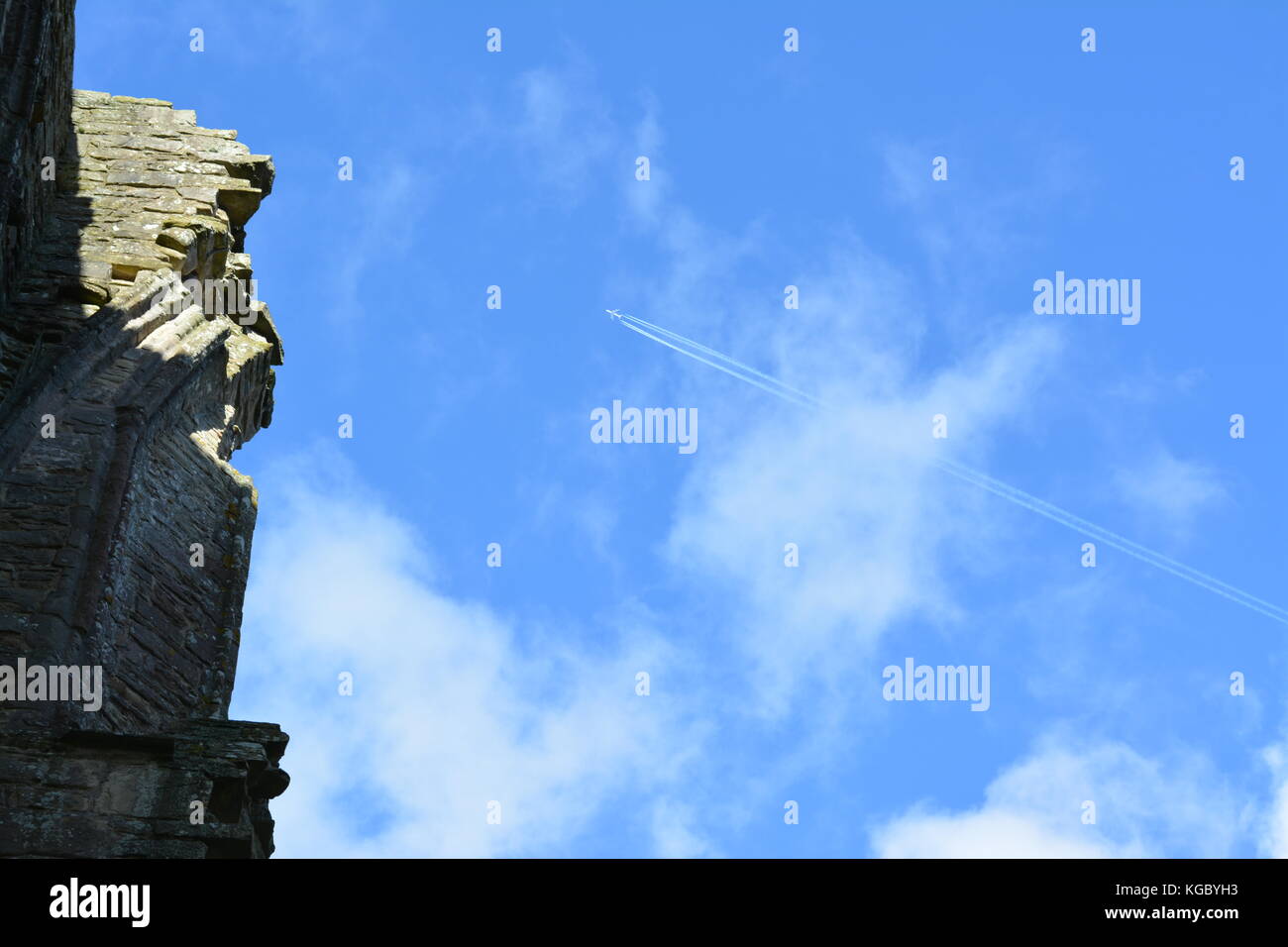 Sunny autunnale di cielo blu con nuvole wispy mostrando aereo passeggeri e sentieri di vapore sorvolano le rovine del vecchio monastero Abbazia di Tintern monmouthshire Foto Stock