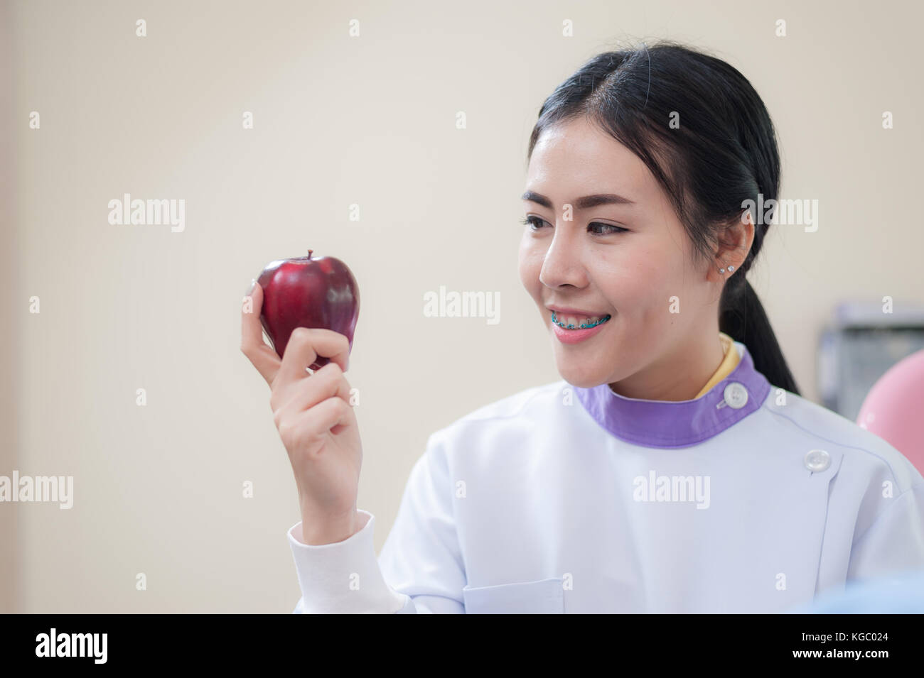 Dentista femmina azienda mela rossa in mano mentre in piedi di fronte ad apparecchiature dentali e dispositivi in clinica. heath care e il concetto di manutenzione Foto Stock