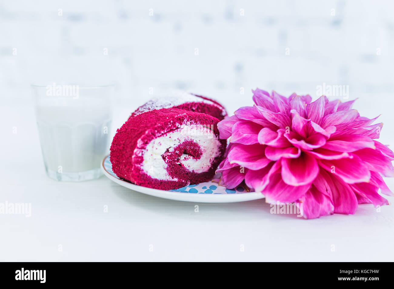 Una torta rossa del velluto rotolo tagliato con tazza di latte e fiori. sfondo bianco. Foto Stock