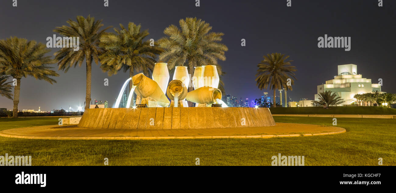 Doha, skyline del Qatar di notte che mostra il Museo d'arte islamica, fontana del vaso d'acqua, alberi e grattacieli sullo sfondo. Foto Stock