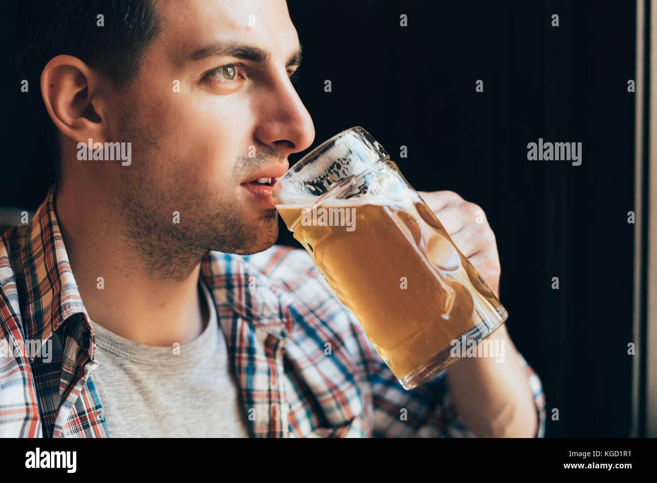 Persone, bevande, alcol e il concetto di tempo libero - chiusura del giovane uomo beve birra dal vetro al bar o pub Foto Stock