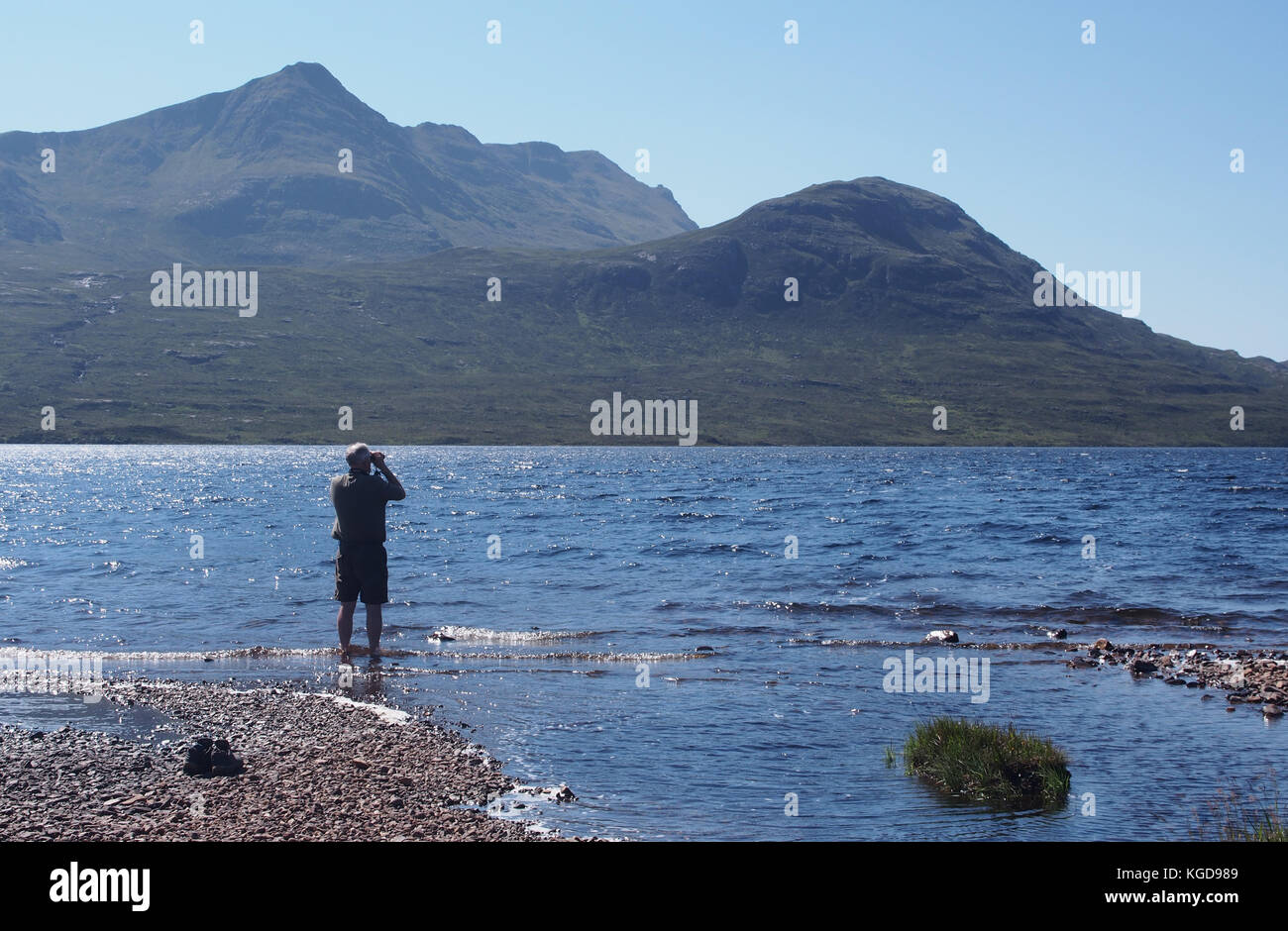 L'uomo paddling, guardando attraverso il binocolo attraverso Lochan Fada a munro Slioch, Scozia Foto Stock