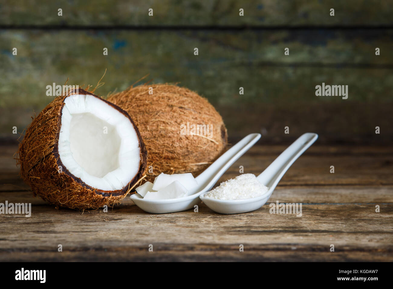 Tutto fresco tagliato a metà noci di cocco con scaglie di noce di cocco e trita in cucchiai su sfondo di legno con spazio di copia Foto Stock