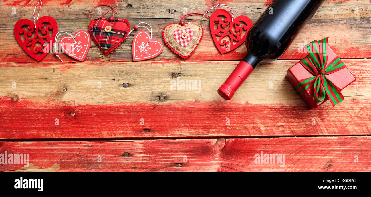 Il giorno di san valentino del concetto. vino rosso bottiglia, una confezione regalo e cuori rossi su sfondo di legno Foto Stock