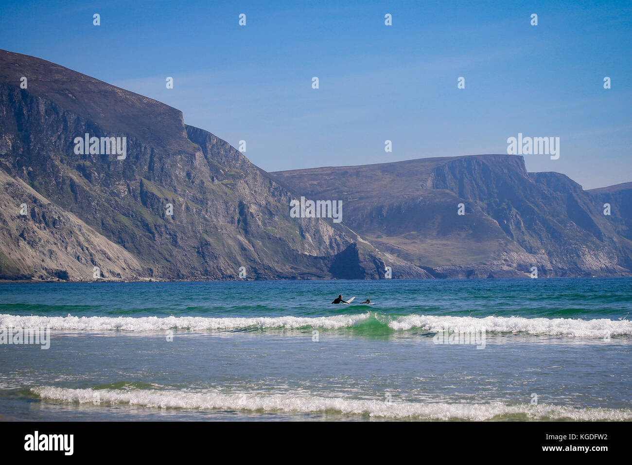 Surfers in acqua alla ricerca di onde con spettacolari scogliere minaun in background su una sabbiosa spiaggia di chiglia, Achill Island, nella contea di Mayo, Irlanda Foto Stock