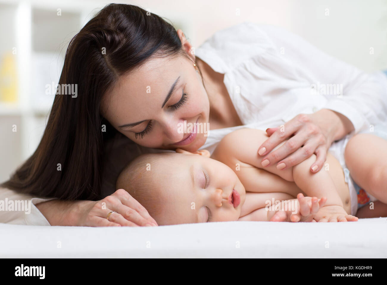 Bella giovane mamma guardando suo sonno bambino più piccolo e sorridente. Bambino giacente nel letto di casa Foto Stock