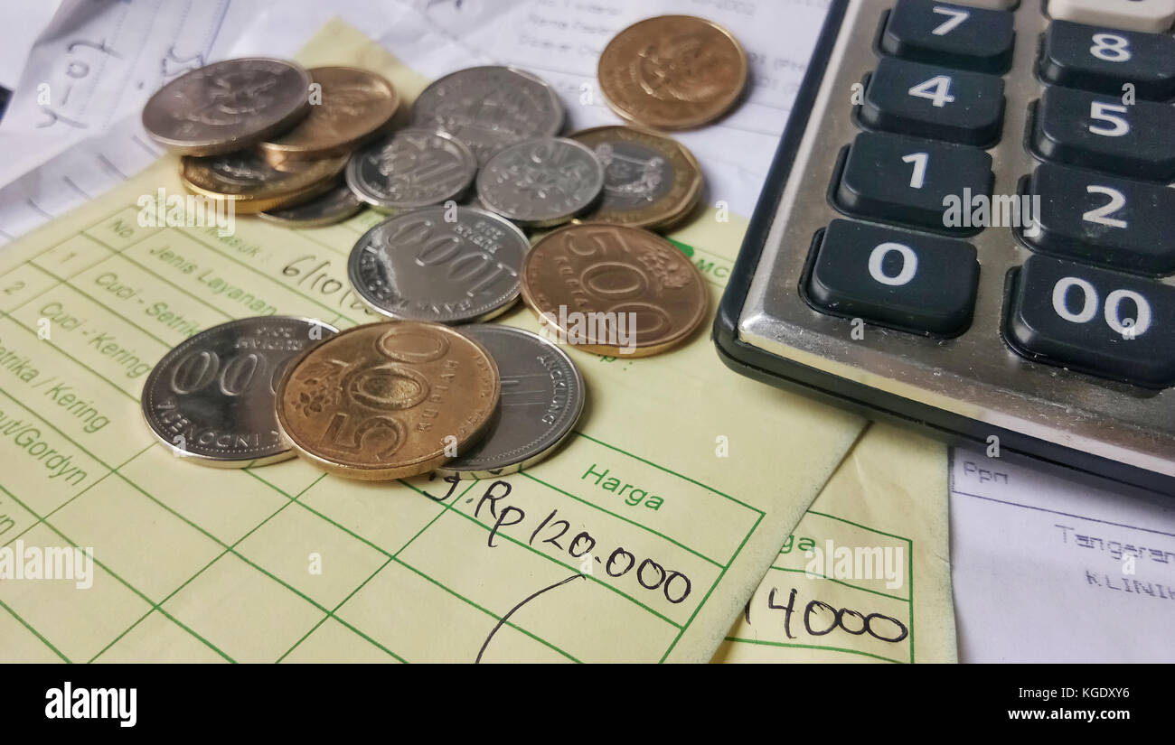 Calcolo della ricevuta di pagamento con vista dall'alto/piatto, con monete in rupia indonesiana e dollari di Singapore, calcolatrice e fatture scritte a mano Foto Stock