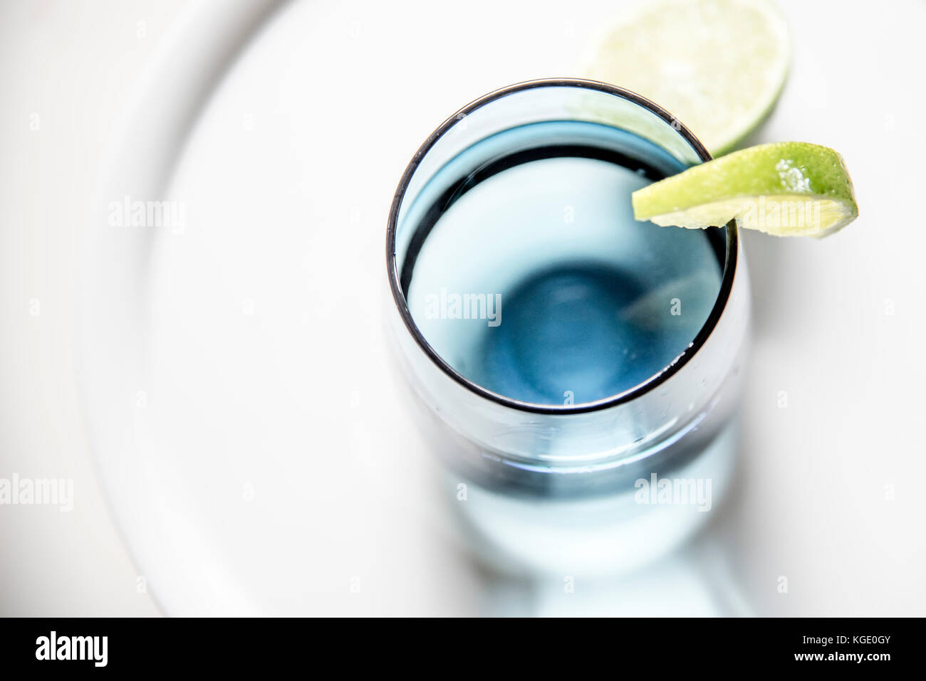 Bicchiere di acqua con fetta di limone, closeup, vista dall'alto. acqua in vetro blu con calce macro, sfondo bianco, orizzontale. Foto Stock