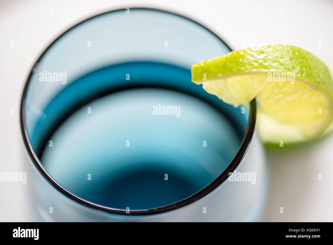Bicchiere di acqua con fetta di limone, closeup, vista dall'alto. acqua in vetro blu con calce macro, sfondo bianco, orizzontale. Foto Stock