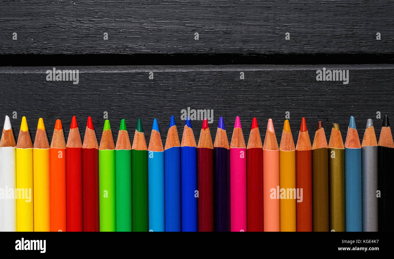 Colorate matite colorate su di un legno nero, sfondo allineati su un gradiente arcobaleno Foto Stock
