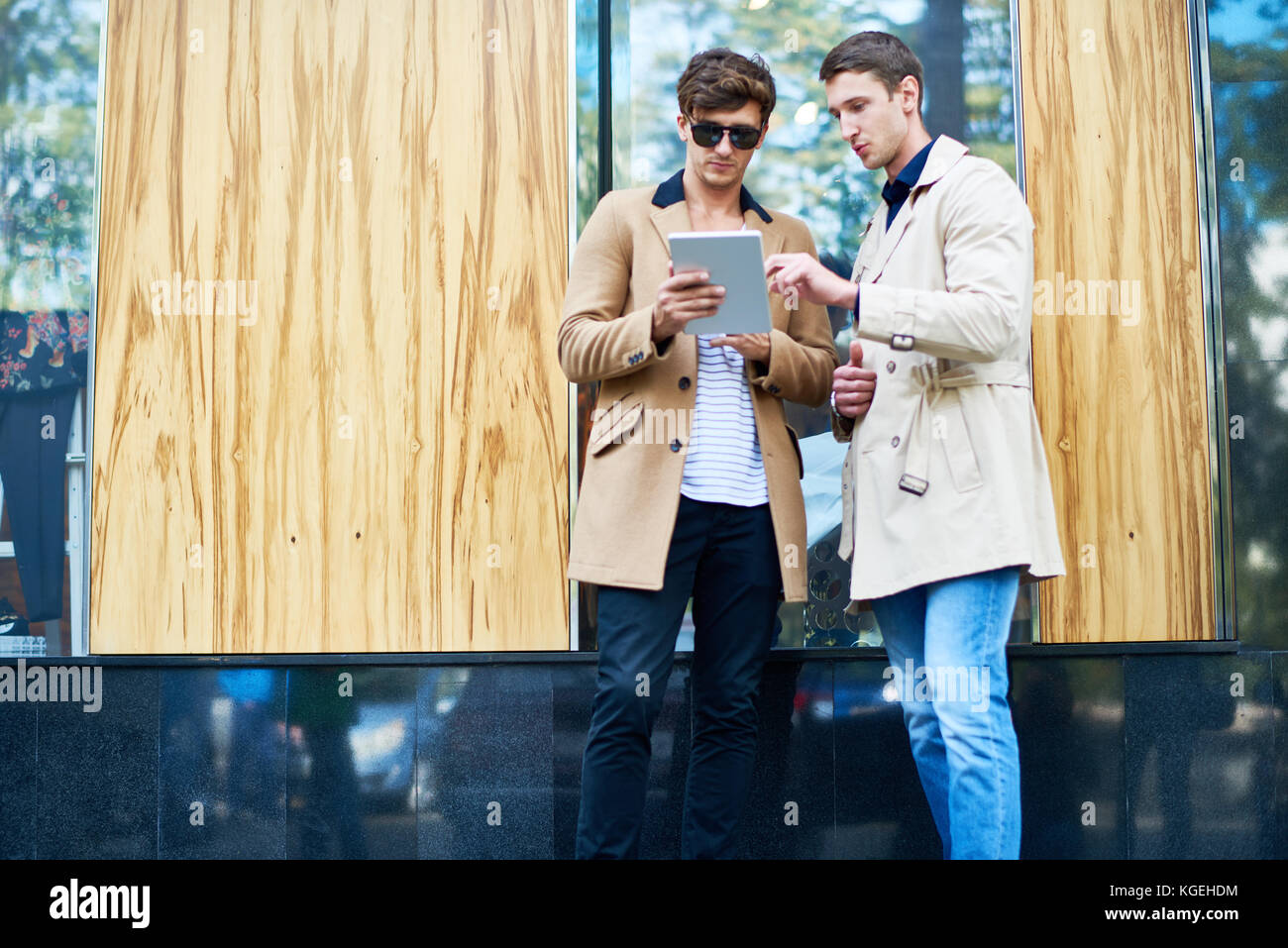 Ritratto di due giovani uomini con tavoletta digitale navigando in rete in piedi all'aperto in autunno una strada di città, spazio di copia Foto Stock