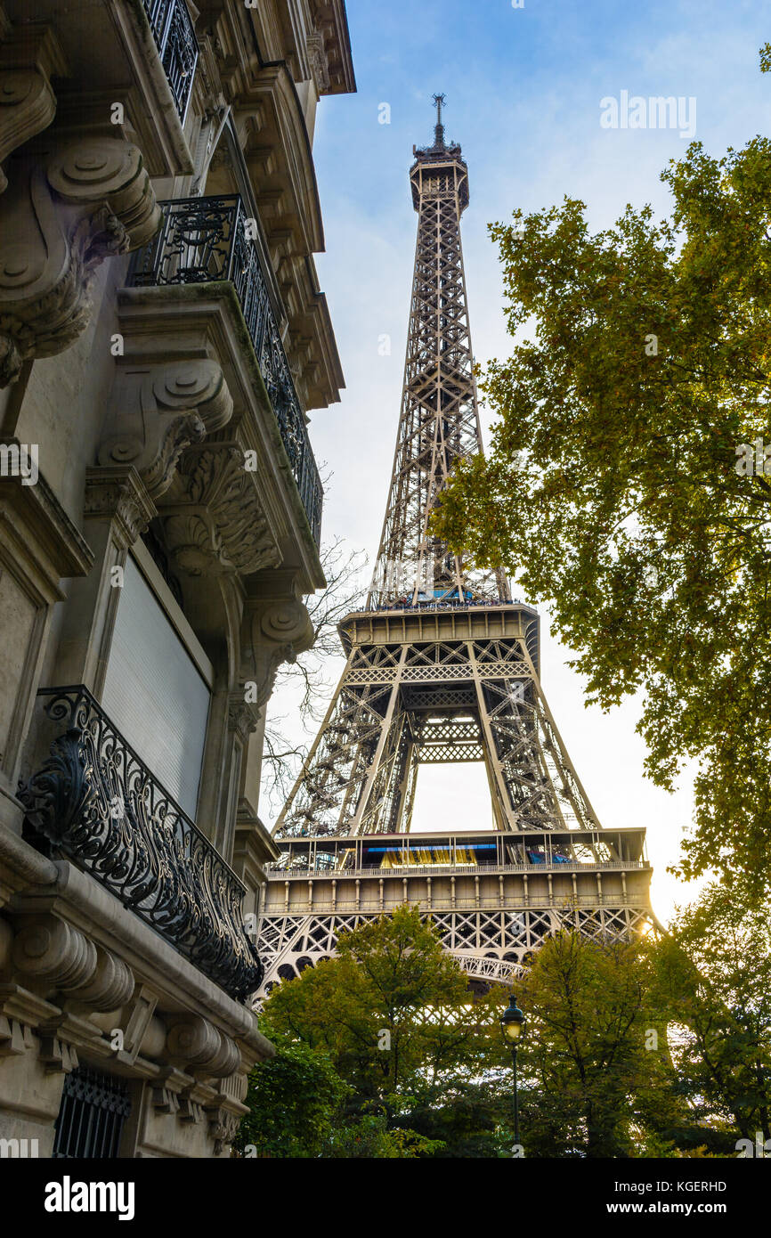 Vista della maestosa torre Eiffel nelle sue immediate vicinanze con alberi e i tipici edifici Parigini in primo piano. Foto Stock