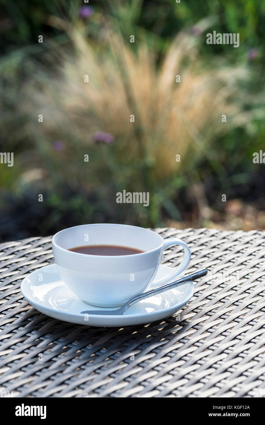 Tazza e piattino caffè tavolo rattan giardino. Foto Stock