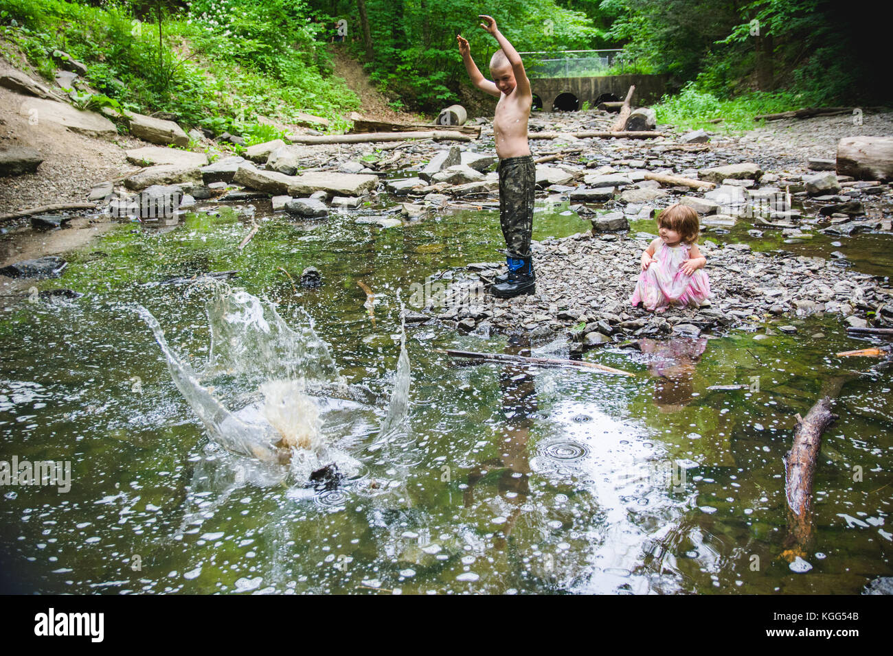 Un 9 anno vecchio ragazzo getta una roccia in un flusso in estate in Upstate New York mentre un bambino bambina orologi. Foto Stock