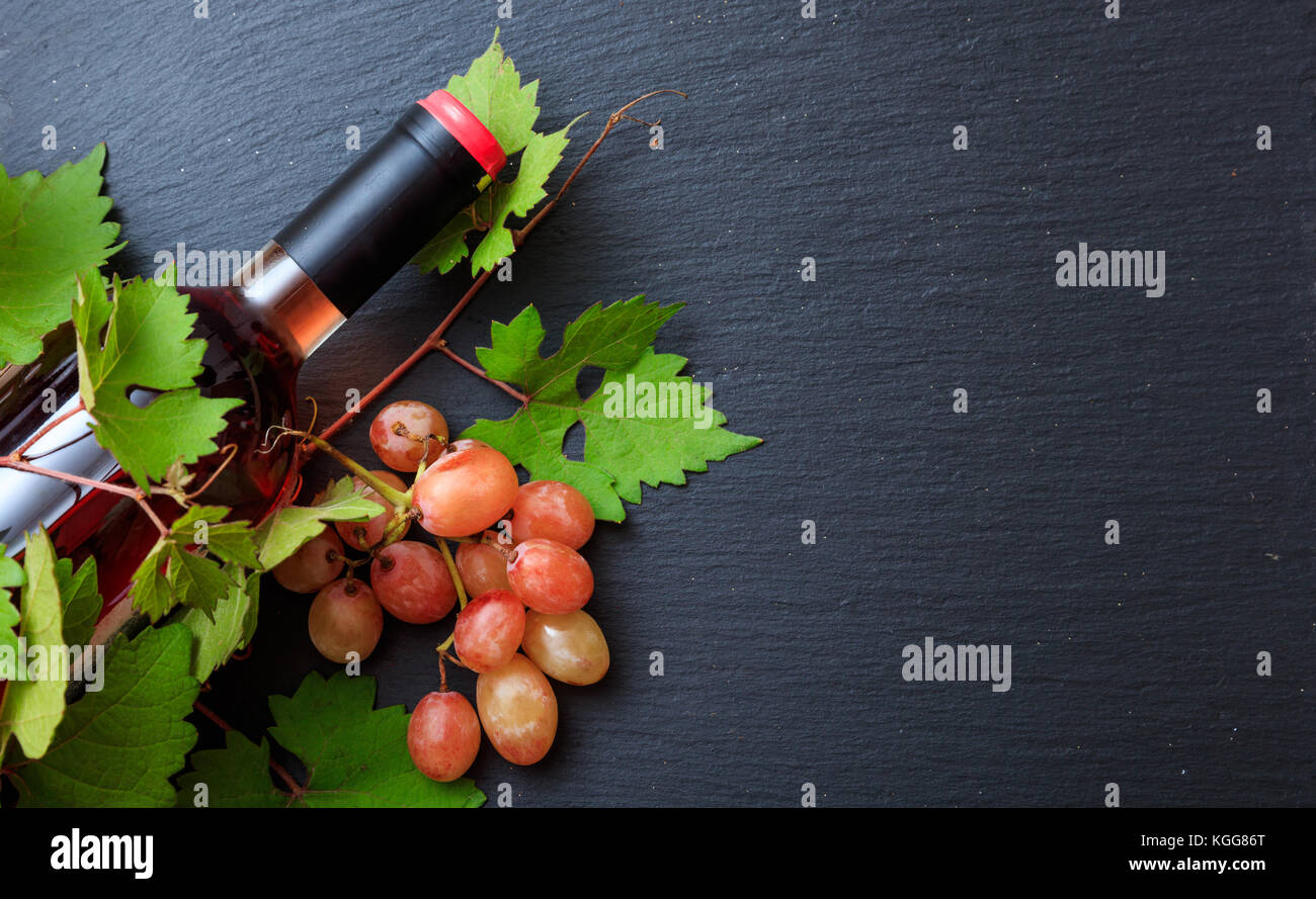 Rose di bottiglie di vino e di uve fresche foglie su sfondo nero, vista dall'alto, spazio di copia Foto Stock