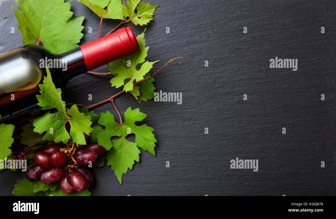 Rosso bottiglia di vino e di uve fresche foglie su sfondo nero, vista dall'alto Foto Stock