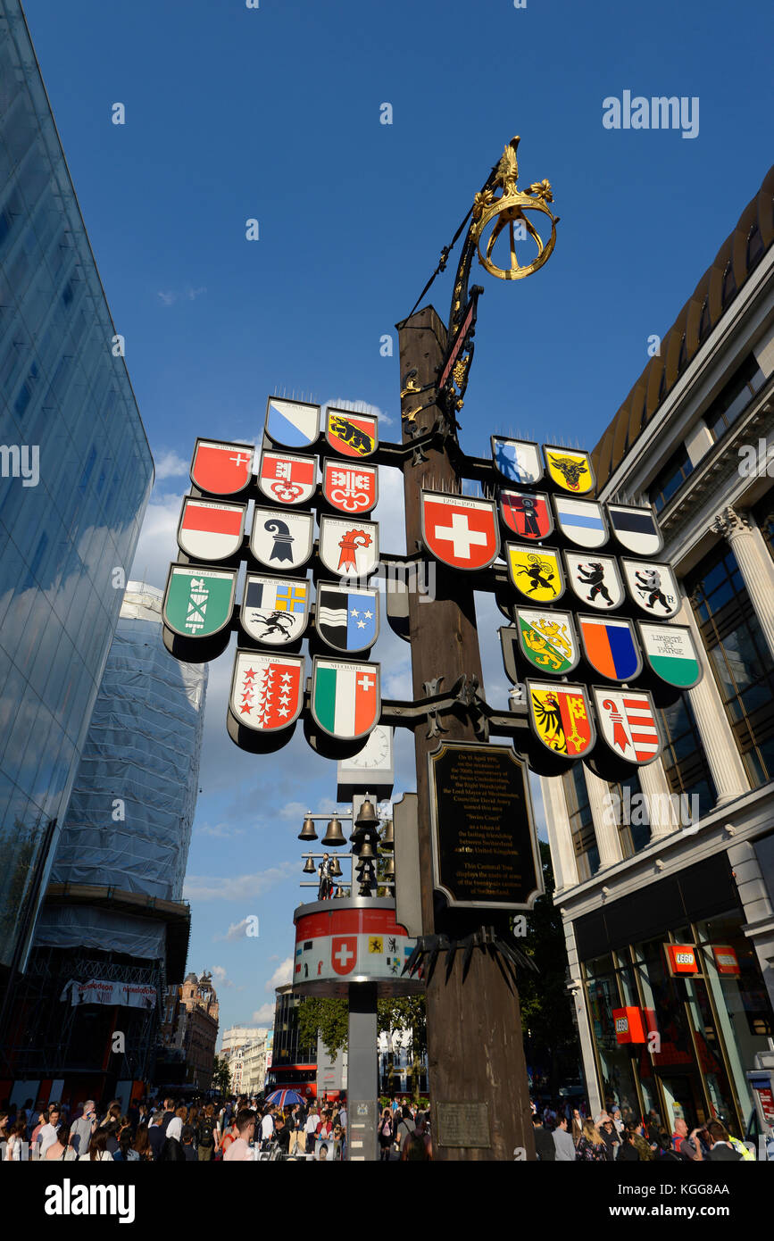 Bandiere di stato della confederazione Svizzera sul palo totem in Swiss Court Leicester Square, Londra, con Glockenspiel Foto Stock