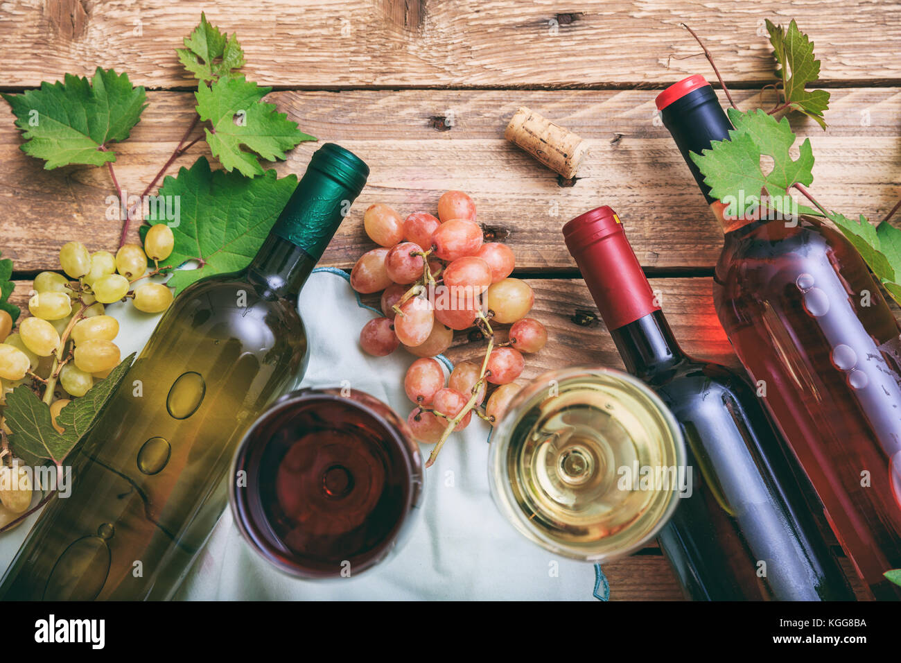 Vino rosso e bianco di bicchieri e bottiglie su sfondo di legno. uve fresche e i mosti di uve lascia come decorazione, vista dall'alto Foto Stock