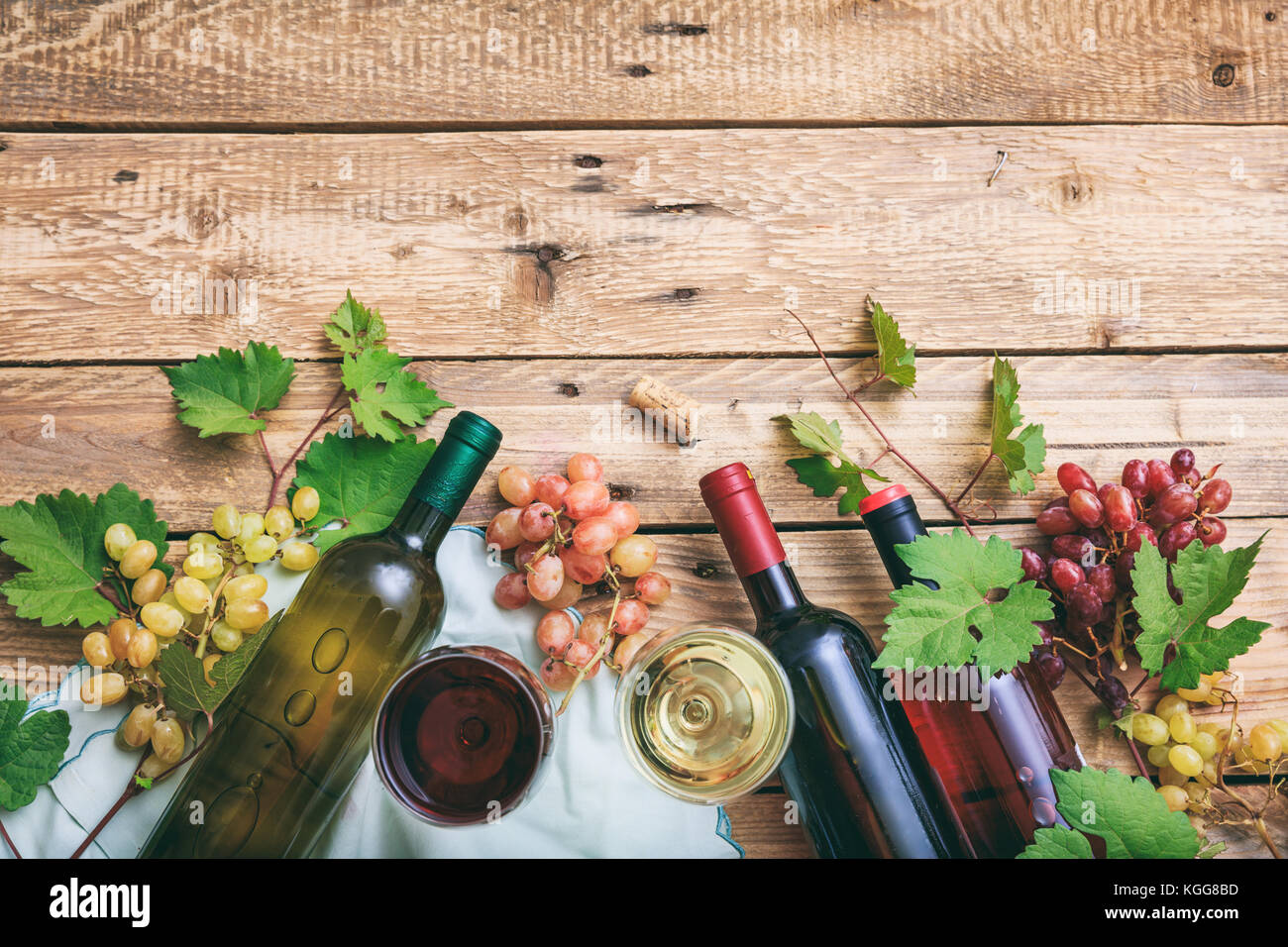 Vino rosso e bianco di bicchieri e bottiglie su sfondo di legno. uve fresche e i mosti di uve lascia come decorazione, vista dall'alto, spazio di copia Foto Stock
