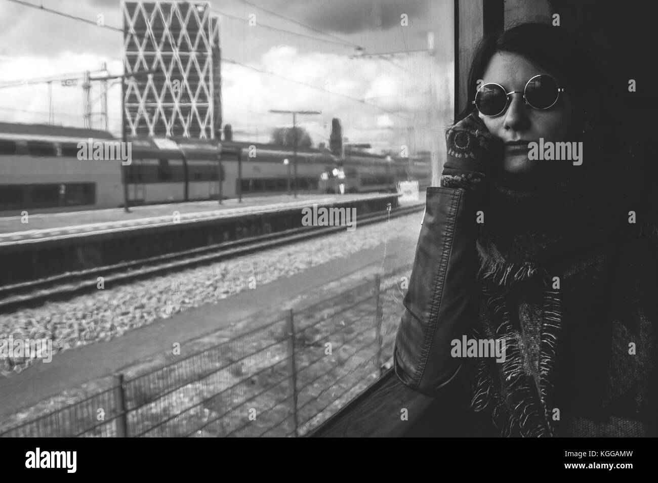 Giovane donna che viaggiano in treno metropolitano, seduta dalla finestra, indossando occhiali da sole di Lennon, Amsterdam, Paesi Bassi Foto Stock