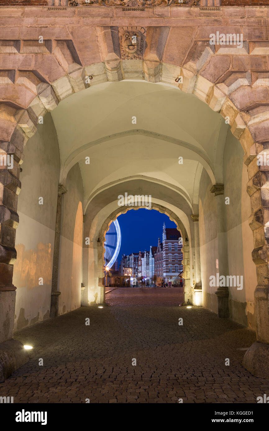 Strada di ciottoli e illuminato gateway presso lo storico cancello verde presso le principali città della Gdansk, Polonia, la sera. Foto Stock