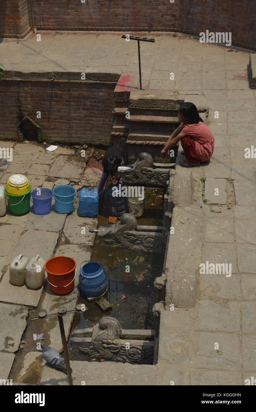Ragazza nepalese in attesa di raccogliere acqua potabile con jerrycan in antica fontana, Kathmandu, Nepal. scarsità d'acqua, siccità, dopo il terremoto Foto Stock