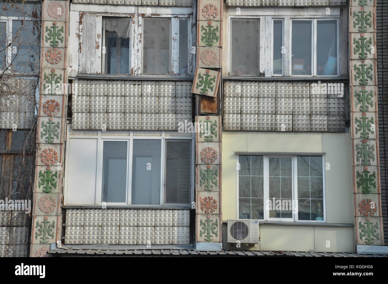 Vecchie piastrelle decorate cadono fuori dalla facciata da un vecchio edificio di appartamenti sovietici in Kakakakhstan. rifiuta. costruzione rapida. caduta a parte, ancora in uso, facciata Foto Stock