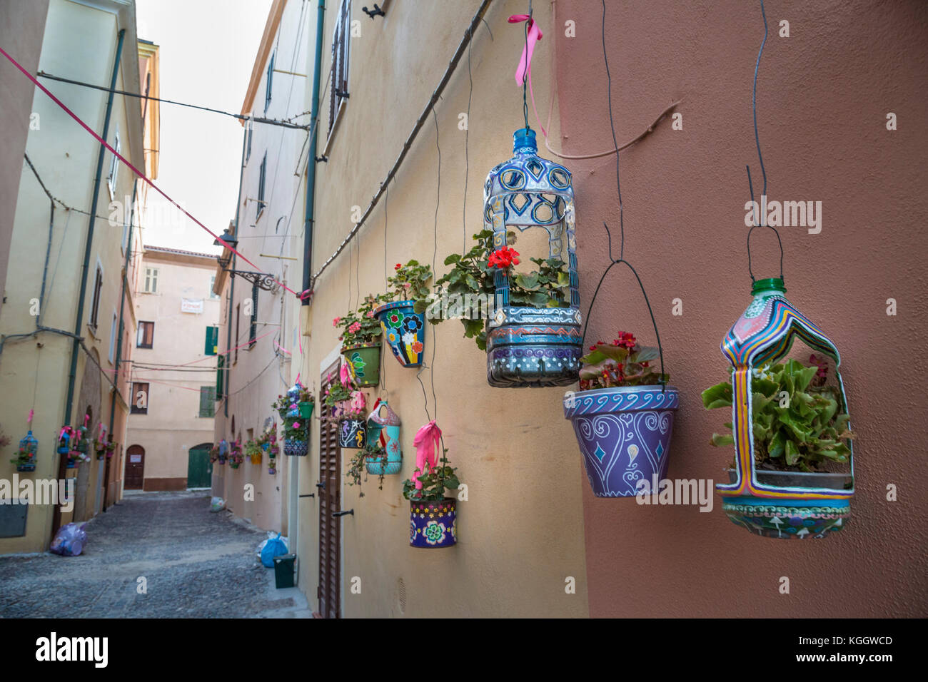 Fiori in decorate a mano appesa fioriere fodera una stretta di ciottoli pietra vicolo di Alghero, Sardegna Foto Stock