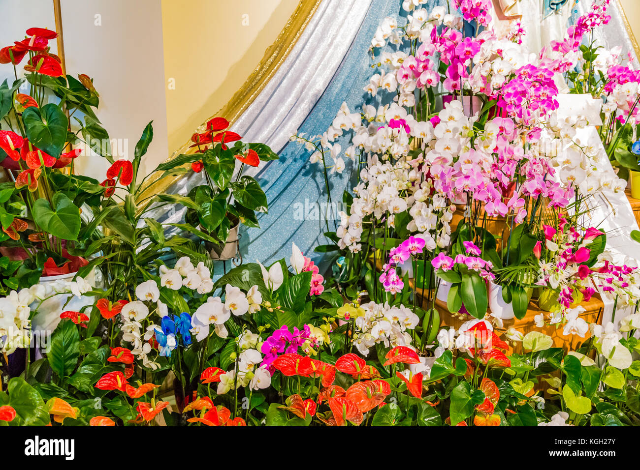 Composizione floreale di rose e orchidee ai piedi di una statua di carattere religioso Foto Stock