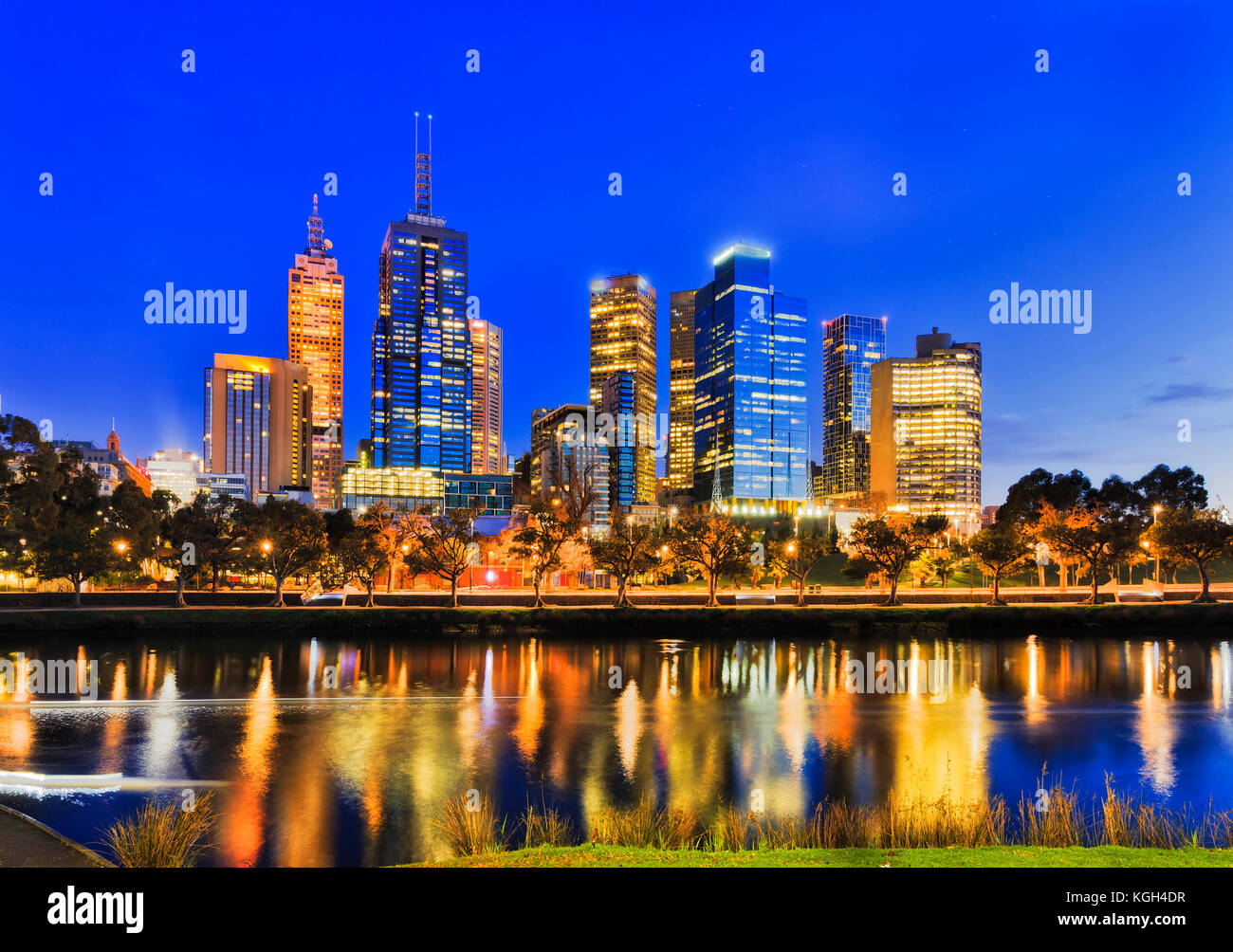 Sunrise scuro nella città di Melbourne attraverso acque del fiume Yarra al lungomare della città CBD quando alto ufficio torri riflettere con luci luminose. Foto Stock