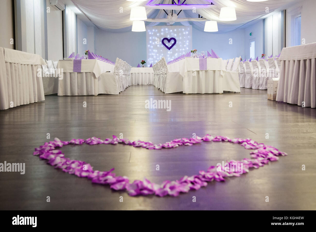 Foto di matrimonio ricevimento sala decorata in viola e bianco colori. in primo piano vi è una pista da ballo con una rosa di petali di fiori forma di cuore . d Foto Stock