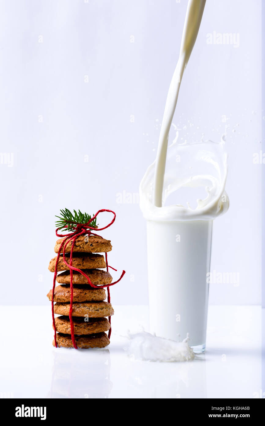 Versare il latte in un bicchiere con schizzi, pan di zenzero biscotti di Natale. Inverno sfondo bianco, vacanze decorazione. Foto Stock